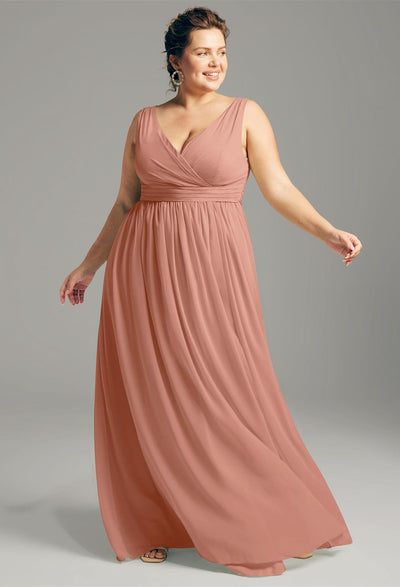 A woman in the Hilaria chiffon bridesmaid dress from Bergamot Bridal, featuring a sleeveless, floor-length design in peach, smiles while looking to the side, exuding an elegance ideal for a bridal shop showcase in London, Ontario.