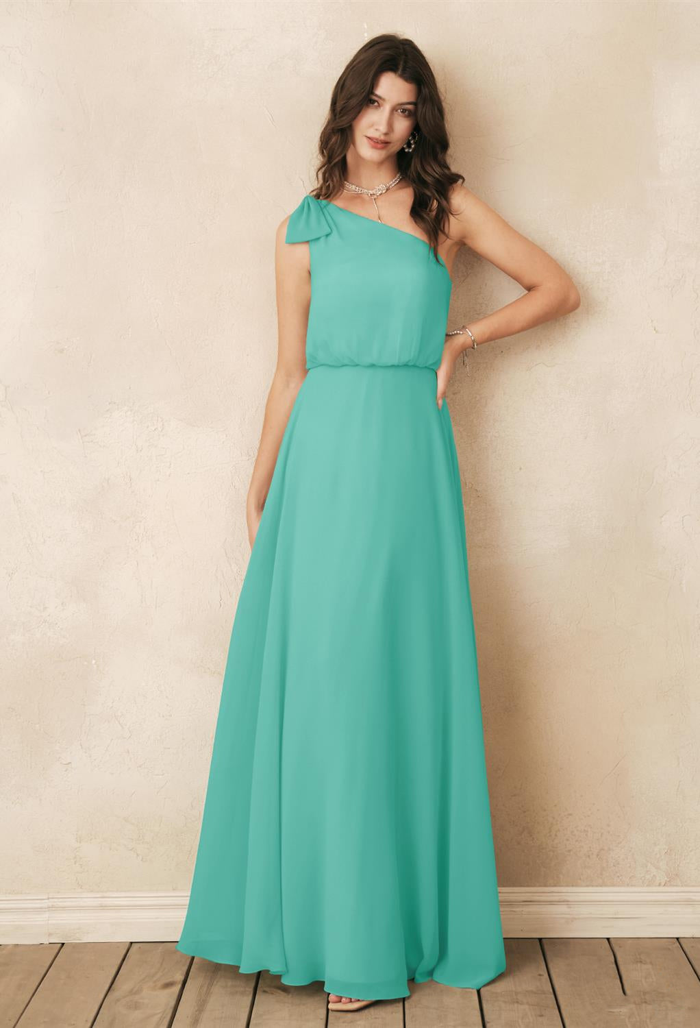 A woman wearing a turquoise bridesmaid dress, the Robina - Chiffon Bridesmaid Dress - Off The Rack from Bergamot Bridal, in a bridal shop.