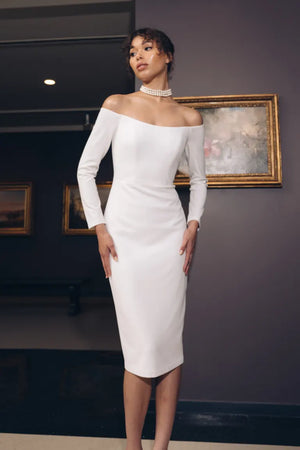 A woman in a white off the shoulder dress posing in an art gallery, showcasing the Ayla - Jenny Yoo Little White Dress by Bergamot Bridal.