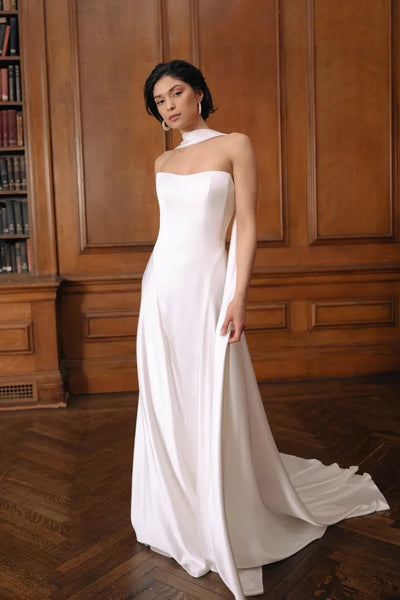 A woman in an elegant Jenny Yoo Wedding Dress gown, fashioned from luxe satin fabric and inspired by old Hollywood, with a subtle train standing in a room with wood paneling.