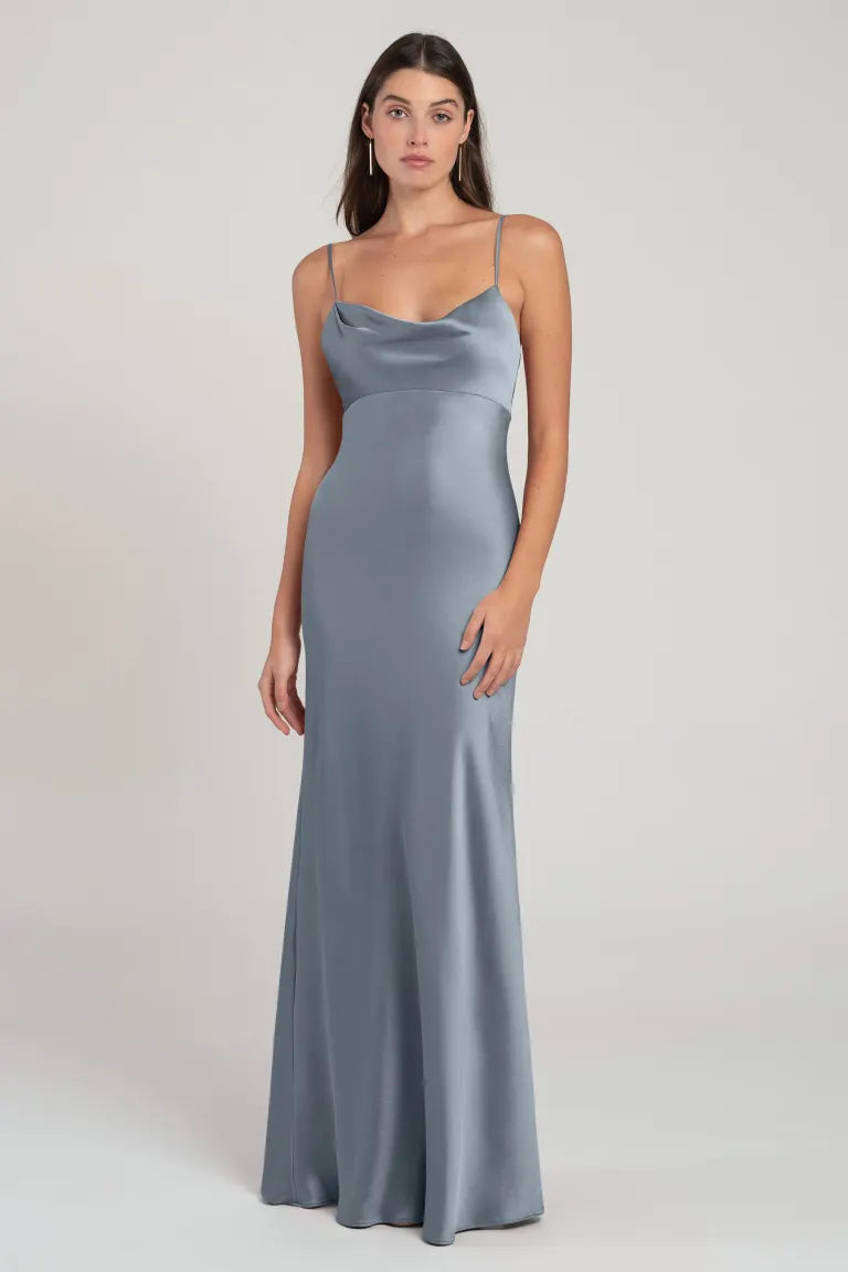 A woman in a sleek, silver satin Addison - Bridesmaid Dress by Jenny Yoo with an empire waist stands poised against a neutral background.