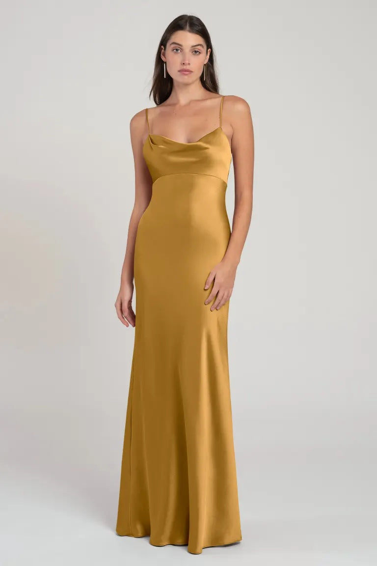 A woman wearing an elegant gold satin evening gown with an empire waist, the Addison Bridesmaid Dress by Jenny Yoo from Bergamot Bridal.