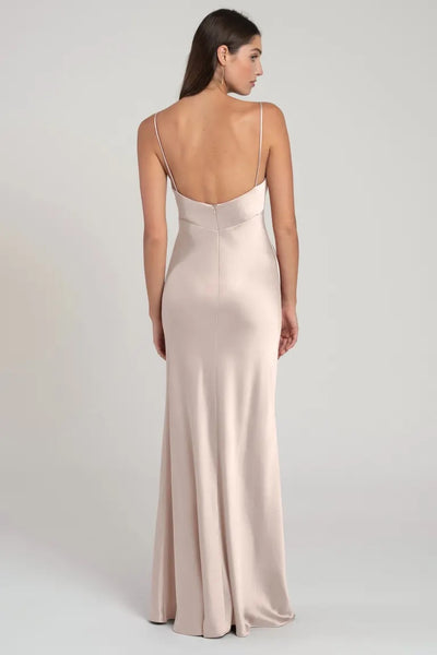 Woman modeling a pale pink, satin slip evening gown with slender straps and a flared hem from a rear angle from Bergamot Bridal's Addison - Bridesmaid Dress by Jenny Yoo.