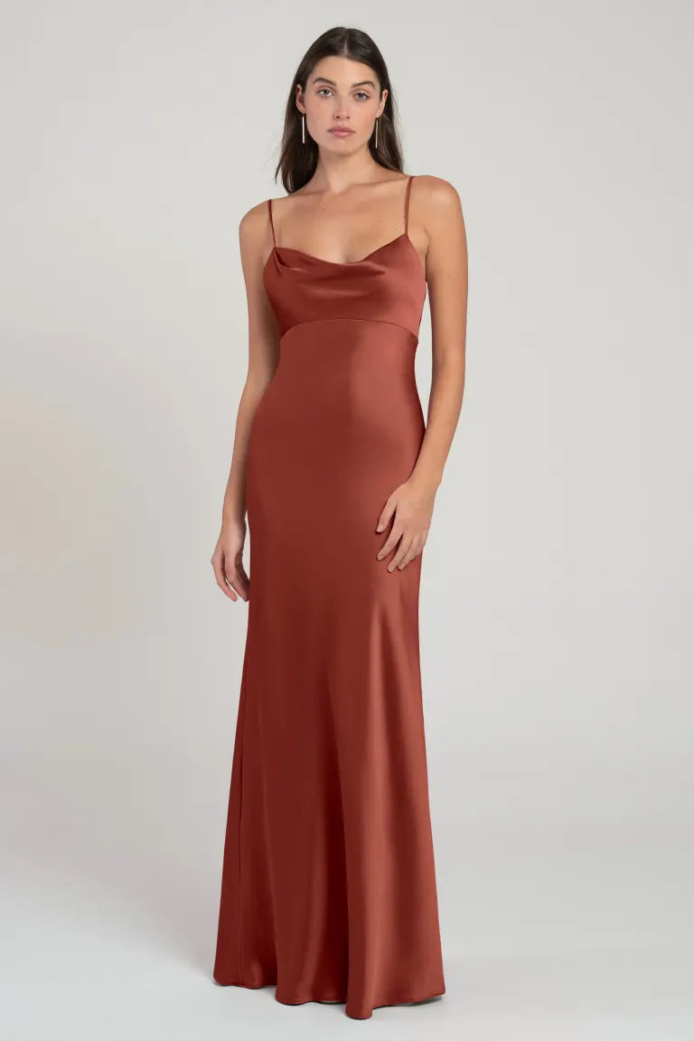 Woman posing in a sleek, rust-colored satin Addison bridesmaid dress by Jenny Yoo with an empire waist from Bergamot Bridal.
