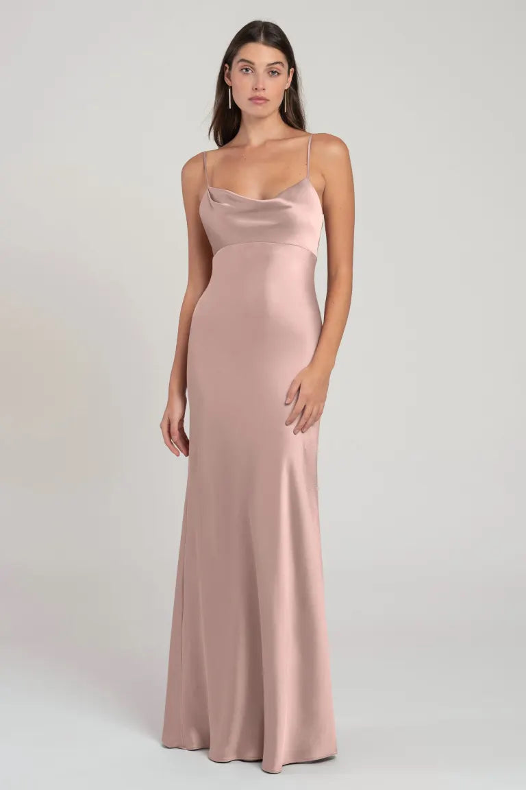 Woman in a long satin pink bridesmaid dress with an empire waist standing against a neutral background wearing the Addison - Bridesmaid Dress by Jenny Yoo from Bergamot Bridal.