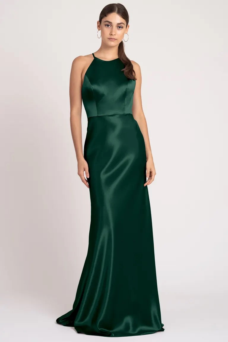 Woman in an elegant green satin back crepe evening gown with a high neckline standing against a neutral background, wearing the Alessia Bridesmaid Dress by Jenny Yoo from Bergamot Bridal.