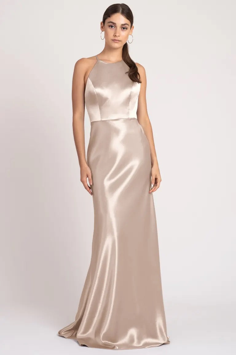 A woman stands posing in a sleek satin back crepe Alessia bridesmaid dress by Jenny Yoo with a high neckline and a neutral tone from Bergamot Bridal.