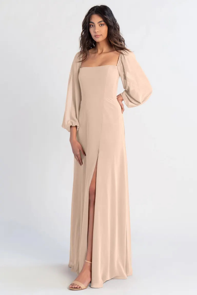 A woman wearing a beige Althea bridesmaid dress by Jenny Yoo with a thigh-high slit and draped chiffon sleeves from Bergamot Bridal.