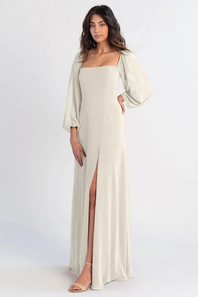 Woman posing in an elegant off-shoulder cream chiffon Bridesmaid dress by Jenny Yoo with a thigh-high slit from Bergamot Bridal.