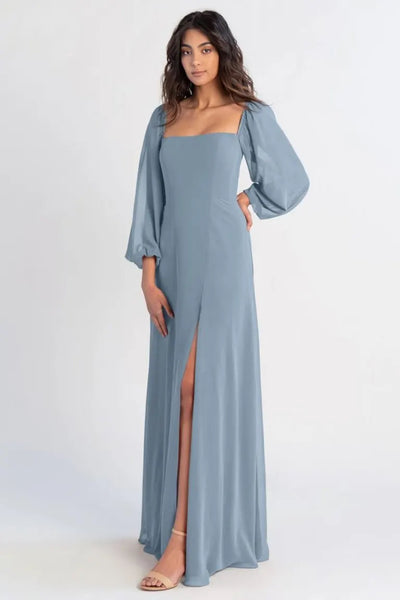 Woman in an Althea - Bridesmaid Dress by Jenny Yoo in Chiffon Blue from Bergamot Bridal with a thigh-high slit, posing against a white background.