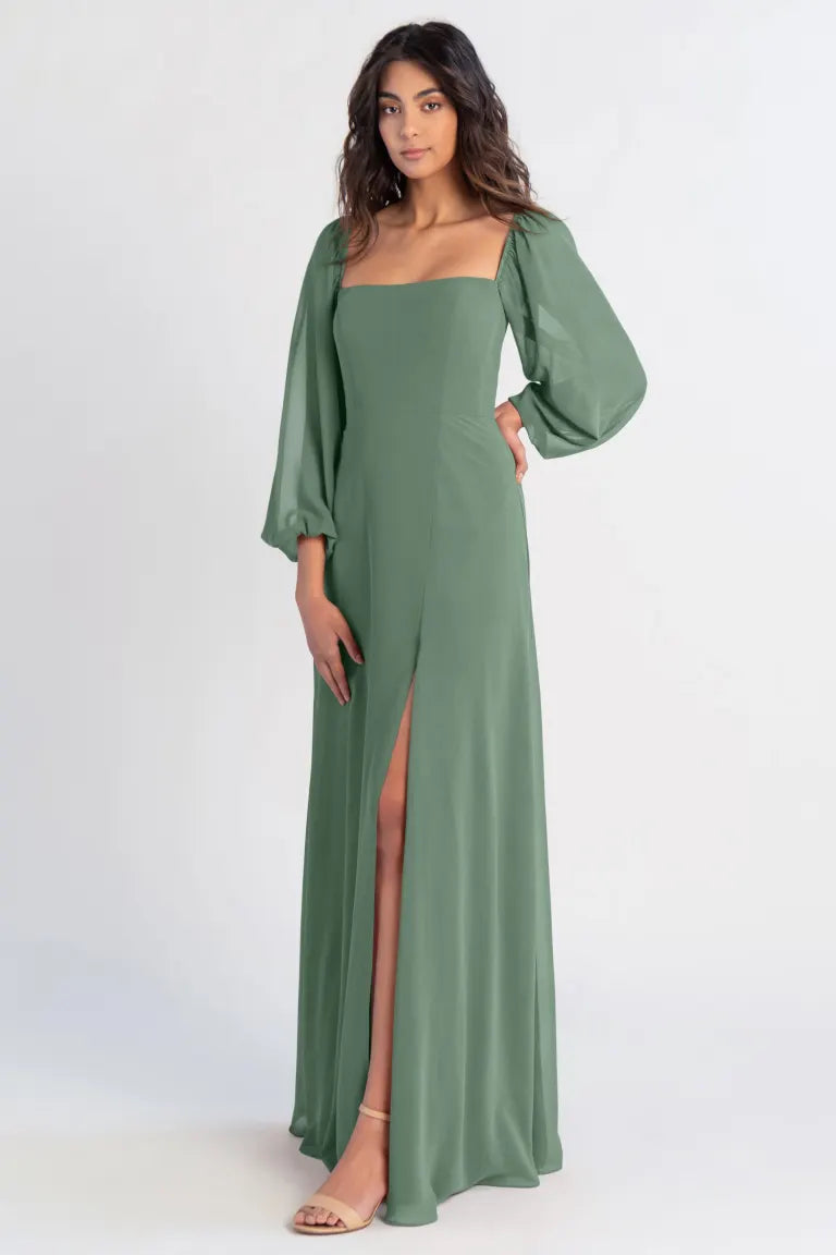 Woman modeling a chiffon green Althea - Bridesmaid Dress by Jenny Yoo with a thigh-high slit, puff sleeves, and an A-line skirt from Bergamot Bridal.