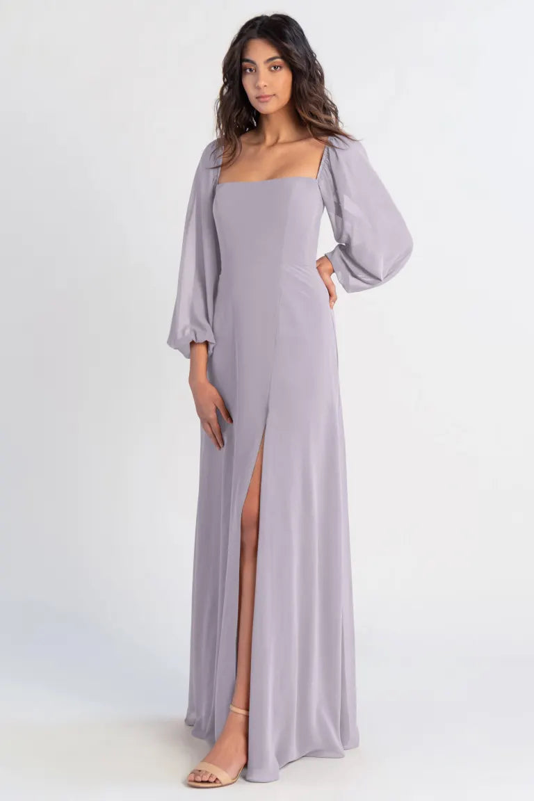 A woman in the elegant Althea - Bridesmaid Dress by Jenny Yoo, from Bergamot Bridal, with a thigh-high slit and puffed sleeves, posing against a plain background.