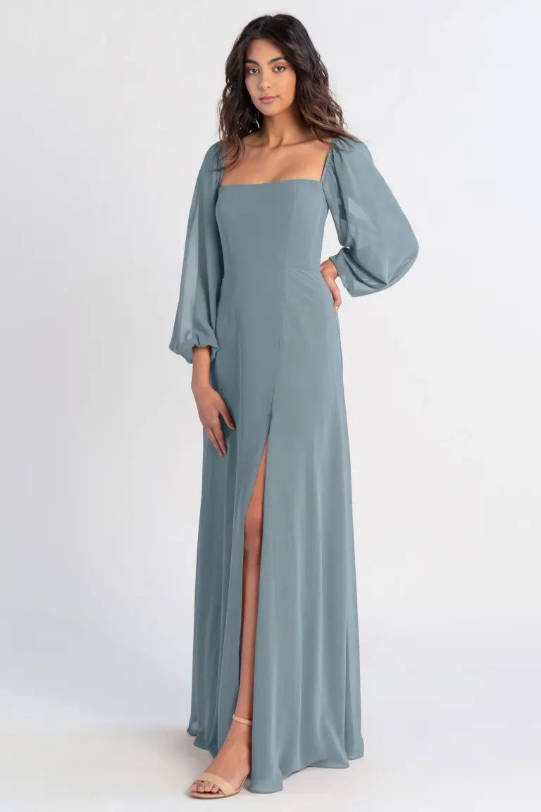 A woman modeling a blue Althea bridesmaid dress with a leg slit and puff sleeves by Bergamot Bridal.