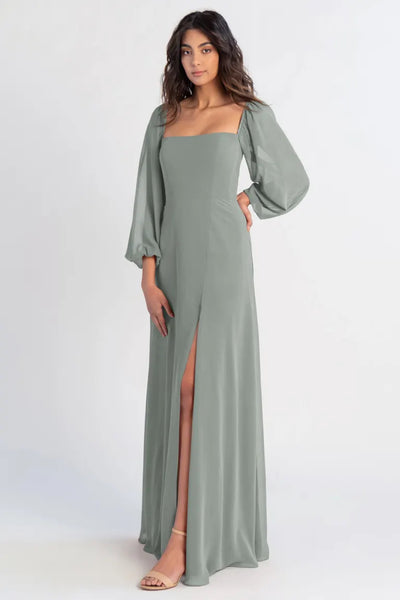 A woman posing in a Althea - Bridesmaid Dress by Jenny Yoo in sage green chiffon with a high slit and lantern sleeves from Bergamot Bridal.