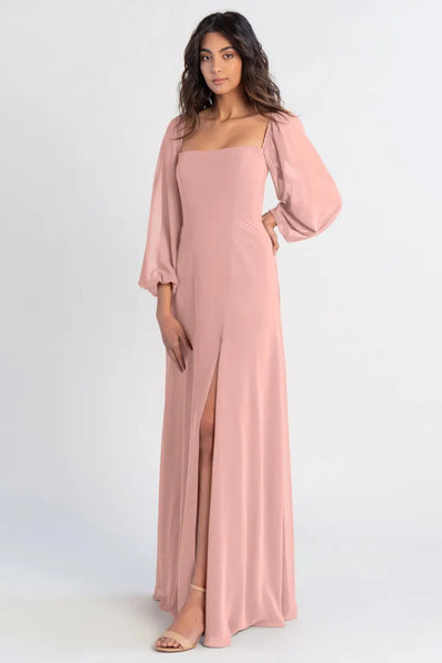 A woman posing in an Althea - Bridesmaid Dress by Jenny Yoo in bohemian pink with a thigh-high slit from Bergamot Bridal.