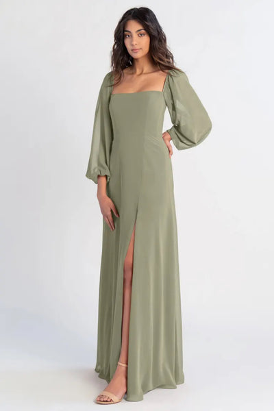Woman posing in a long olive-green chiffon Althea - Bridesmaid Dress by Jenny Yoo with a thigh-high slit and puff sleeves from Bergamot Bridal.