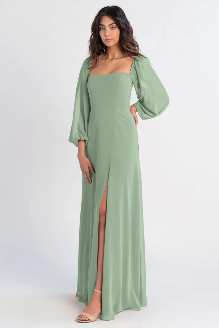 Woman posing in a green chiffon evening dress with a thigh-high slit, the Althea - Bridesmaid Dress by Jenny Yoo from Bergamot Bridal.
