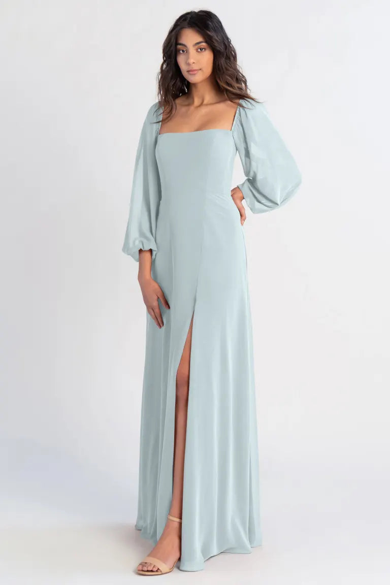Woman in a light blue chiffon Althea bridesmaid dress by Jenny Yoo with a thigh-high slit and A-line skirt posing against a plain background from Bergamot Bridal.