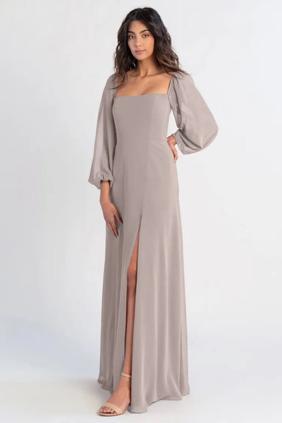 A woman in an elegant Althea - Bridesmaid Dress by Jenny Yoo with a thigh-high slit and flowing sleeves stands against a plain background from Bergamot Bridal.