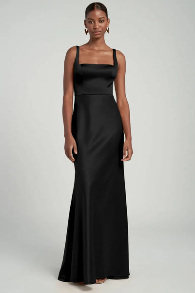 A woman posing in an elegant black satin back crepe Ariana bridesmaid dress by Jenny Yoo with a square neckline from Bergamot Bridal.