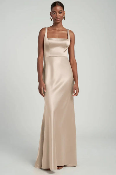 A woman models the Ariana bridesmaid dress by Jenny Yoo from Bergamot Bridal, a long, beige satin back crepe gown with a square neckline.