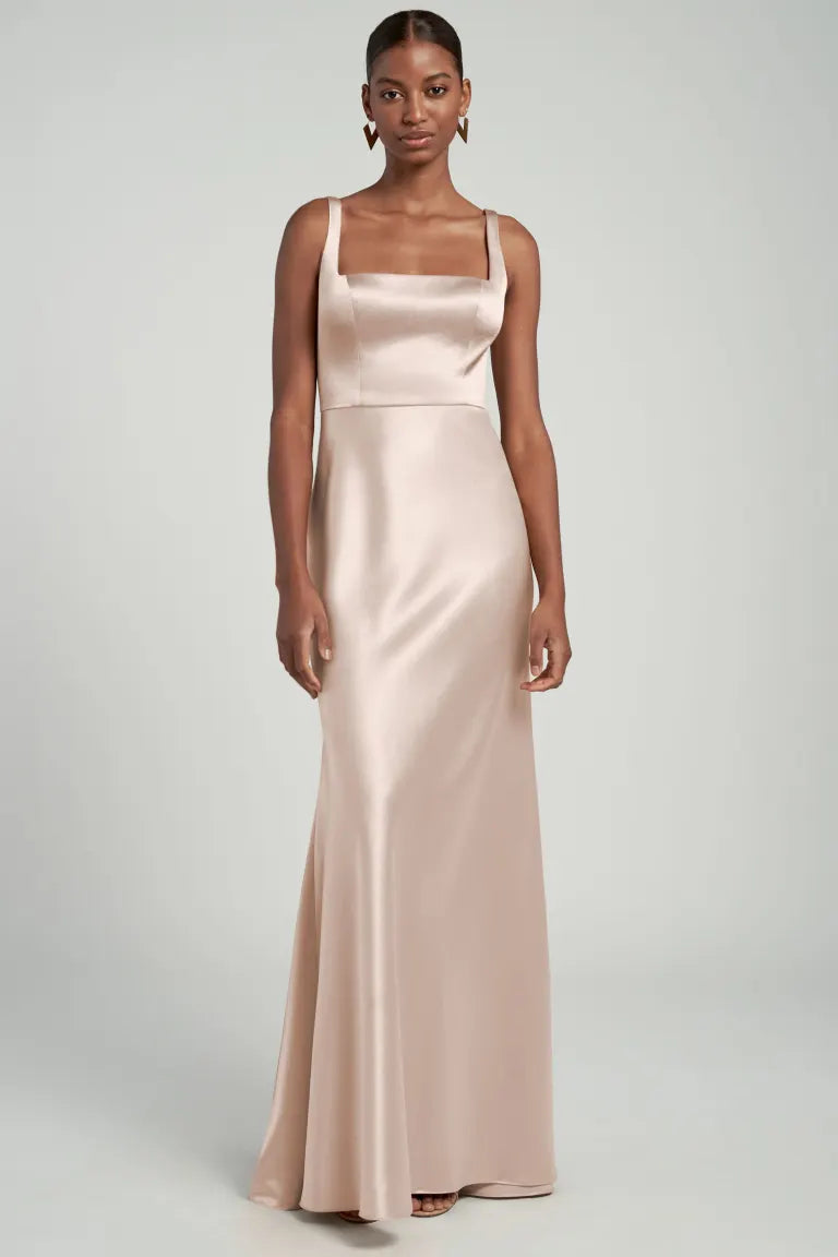 Woman posing in a sleek, pale pink Ariana bridesmaid dress by Jenny Yoo with a square neck from Bergamot Bridal.