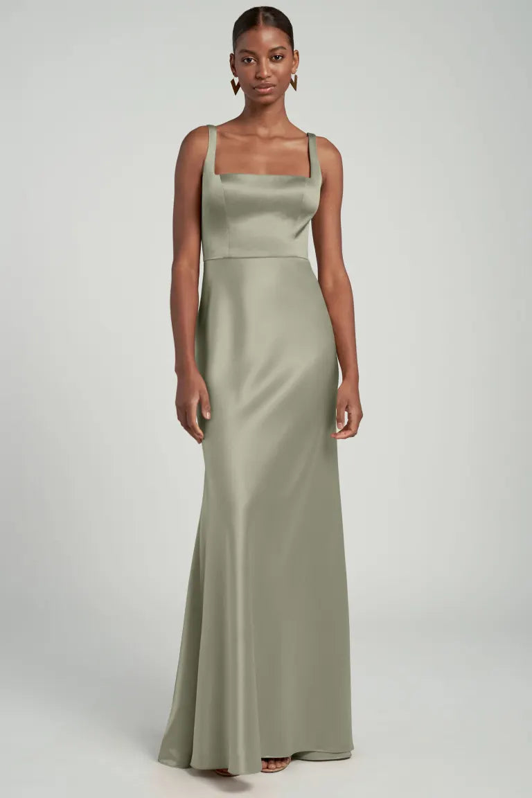 A woman wearing a sleeveless olive green Ariana bridesmaid dress by Jenny Yoo with a square neckline from Bergamot Bridal.