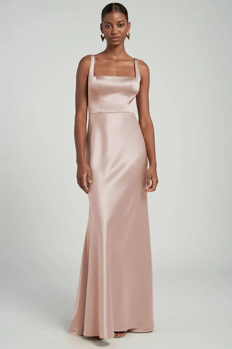 A woman in a sleek, pale pink satin back crepe evening gown with a square neckline designed by Bergamot Bridal's Ariana - Bridesmaid Dress by Jenny Yoo.