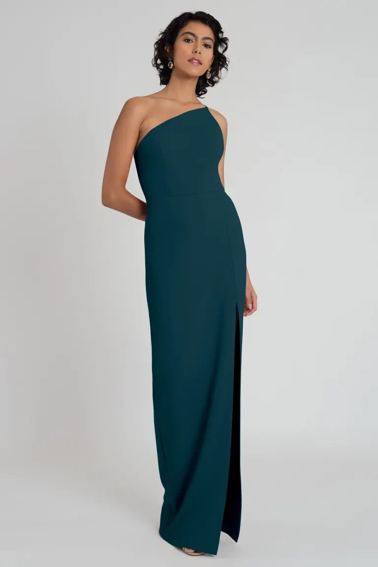 Woman in an elegant teal Aubrey - Bridesmaid dress by Jenny Yoo with a one-shoulder neckline, posing against a neutral background.