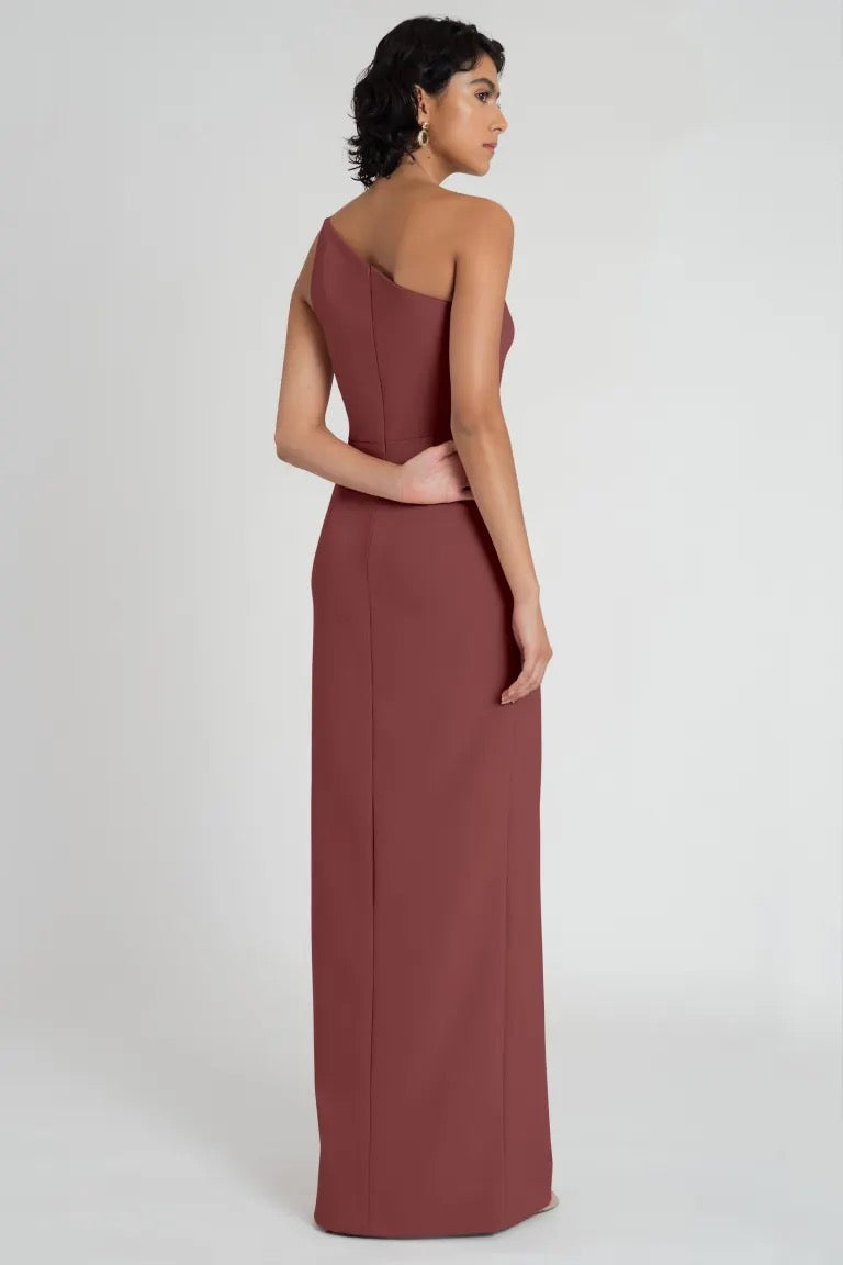 Woman in an elegant maroon Aubrey bridesmaid dress by Jenny Yoo with a one-shoulder neckline, looking over her shoulder from Bergamot Bridal.