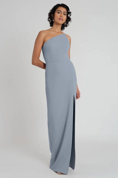 Woman posing in an elegant Aubrey - Bridesmaid Dress by Jenny Yoo with a one-shoulder neckline, crafted from light blue knit crepe from Bergamot Bridal.