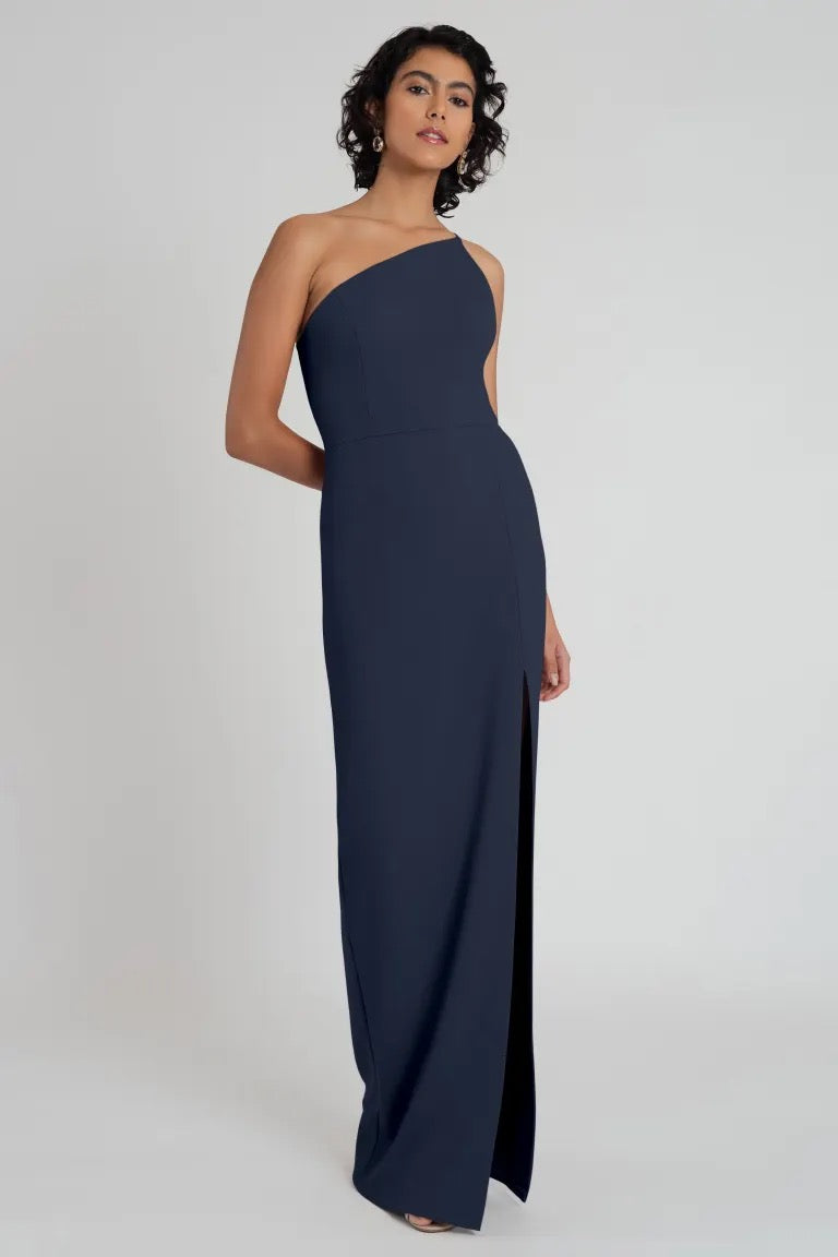 A woman posing in an elegant one-shoulder neckline Aubrey - Bridesmaid Dress by Jenny Yoo made of knit crepe, colored navy blue from Bergamot Bridal.