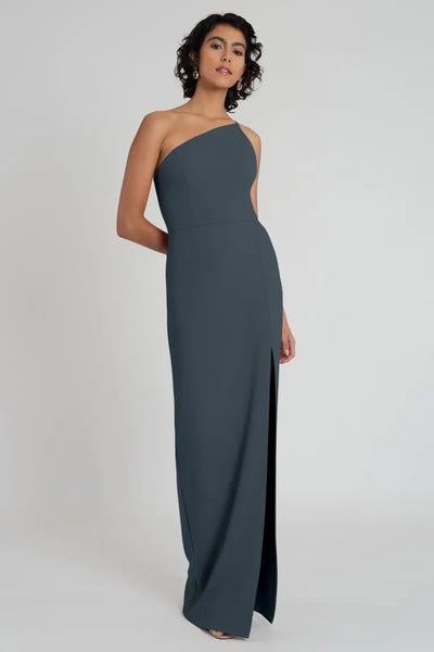 Woman posing in an elegant knit crepe Aubrey - Bridesmaid Dress by Jenny Yoo with a one-shoulder neckline from Bergamot Bridal.