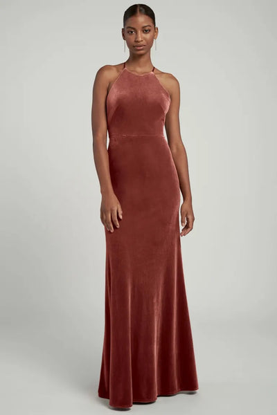 A woman in a long, Bailey - Bridesmaid Dress by Jenny Yoo velvet dress with a halter neckline standing against a neutral background.