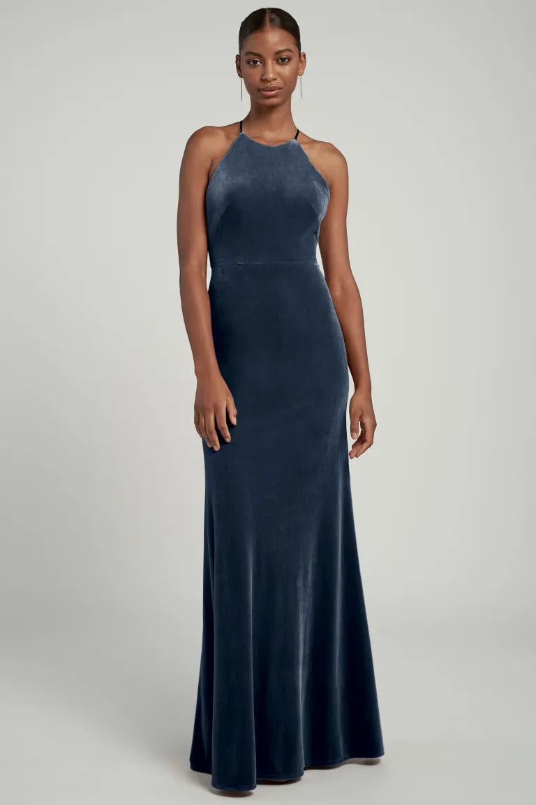 A woman stands posing in an elegant navy blue Bailey velvet dress by Jenny Yoo with a halter neckline from Bergamot Bridal.