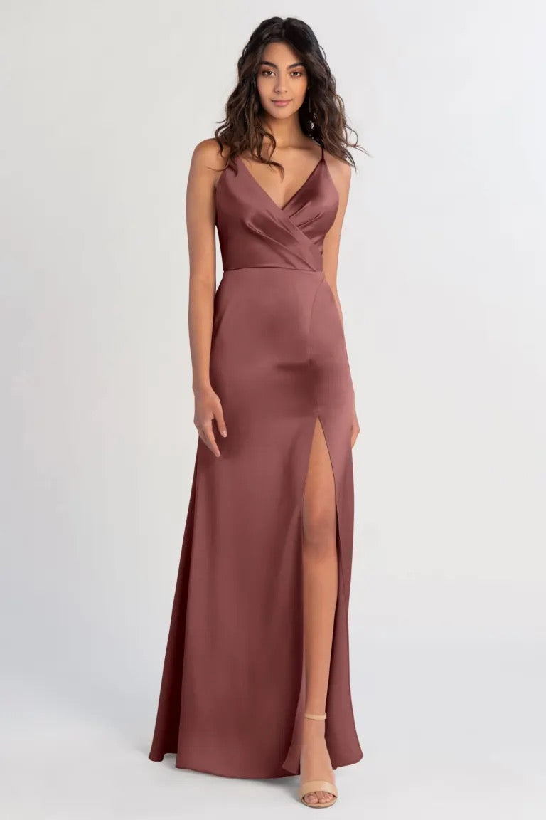 Woman in an elegant burgundy, satin bridesmaid dress with a V-neck and a slit by Bergamot Bridal's Beckette - Bridesmaid Dress by Jenny Yoo.