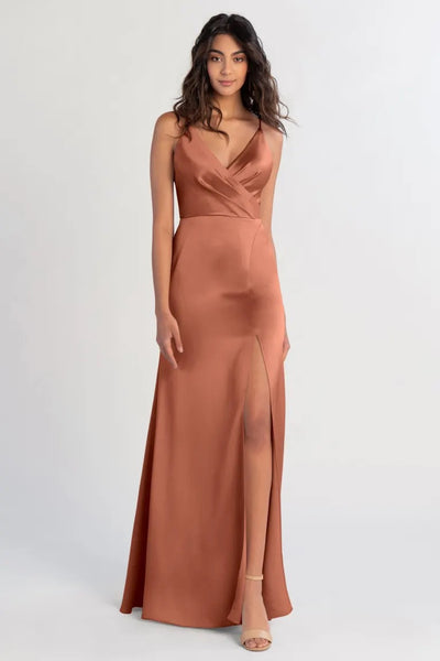 A woman modeling a V-neck satin Beckette bridesmaid dress with a slit by Bergamot Bridal.