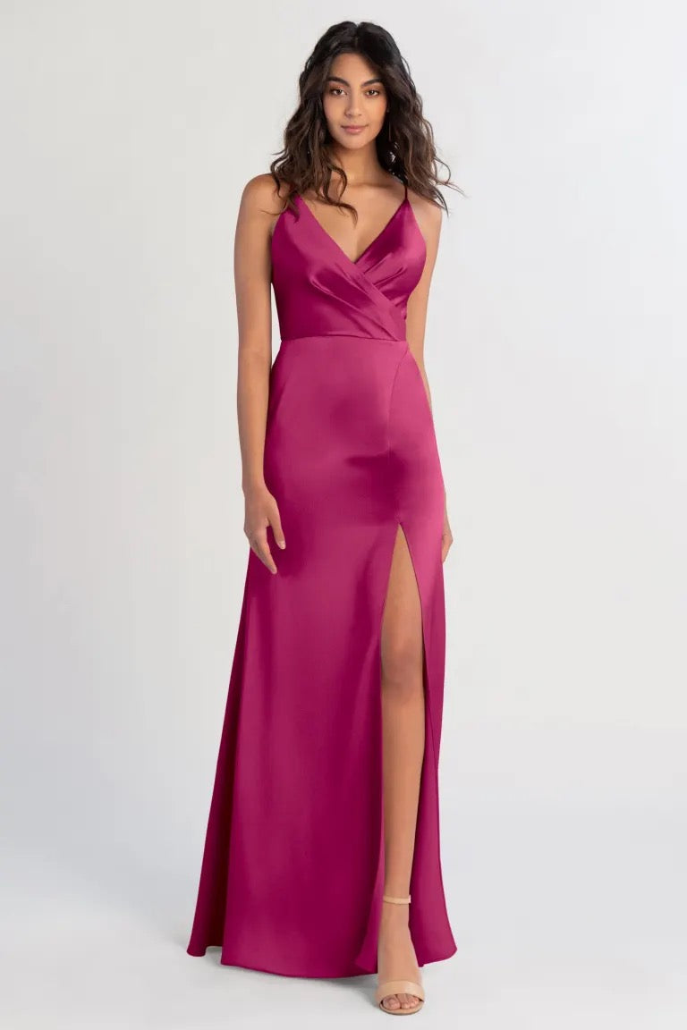 A woman in a pink sleeveless V-neck Beckette bridesmaid dress by Jenny Yoo stands against a plain background.