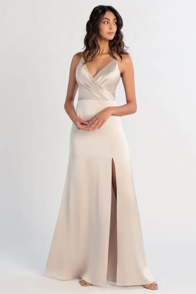 A woman in an elegant Beckette bridesmaid dress by Jenny Yoo with a thigh-high slit posing against a neutral background.