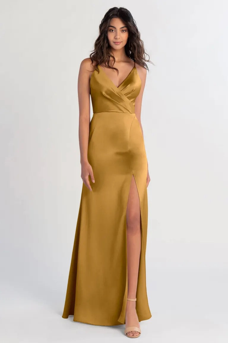 Woman posing in an elegant gold satin bridesmaid dress with a high slit, the Beckette by Jenny Yoo from Bergamot Bridal.