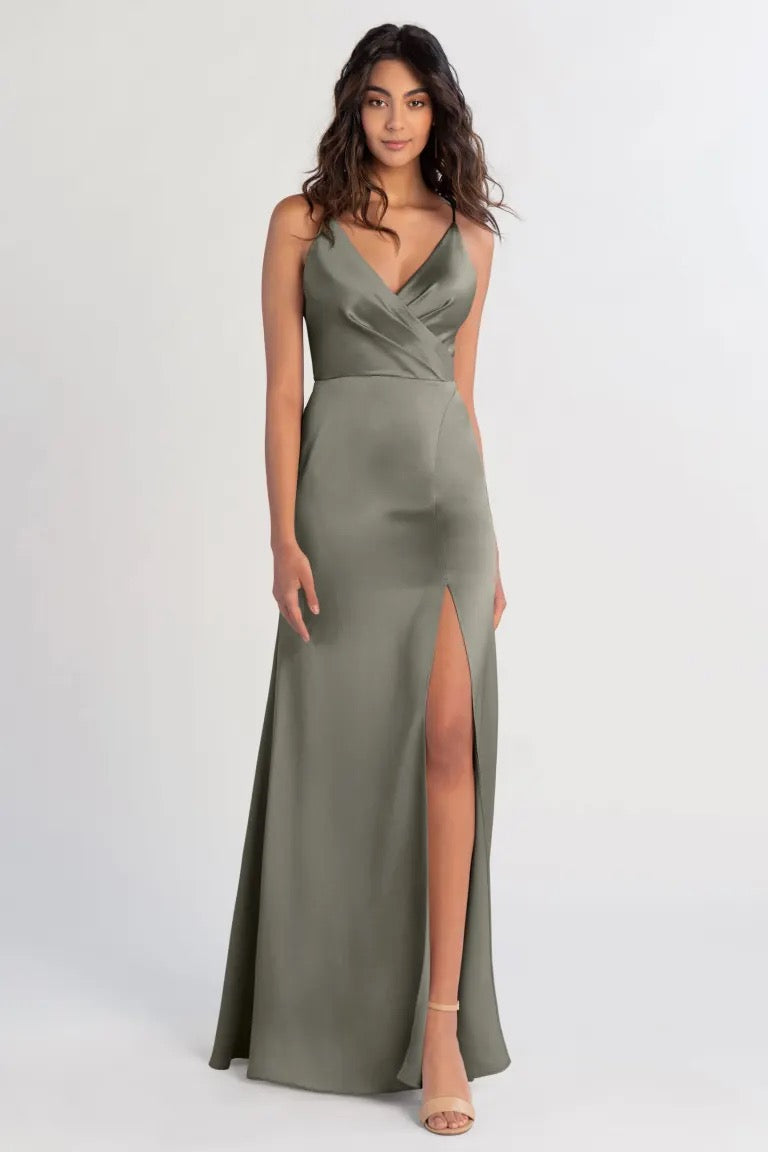 Woman posing in an elegant olive green satin Beckette bridesmaid dress by Jenny Yoo with a high slit from Bergamot Bridal.