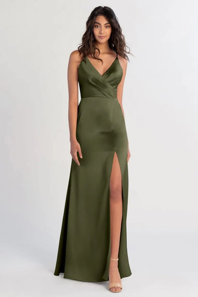 A woman in an olive green satin bridesmaid dress with a Beckette V-neck and a slim A-line skirt stands against a neutral background.
