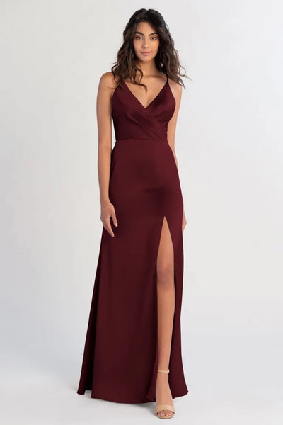 Woman in a burgundy satin evening gown with a thigh-high slit and a V-neck, wearing the Beckette - Bridesmaid Dress by Jenny Yoo from Bergamot Bridal.