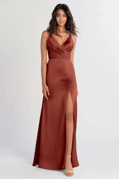 A woman posing in a sleek, russet satin bridesmaid dress with a high slit by Beckette - Bridesmaid Dress from Bergamot Bridal.