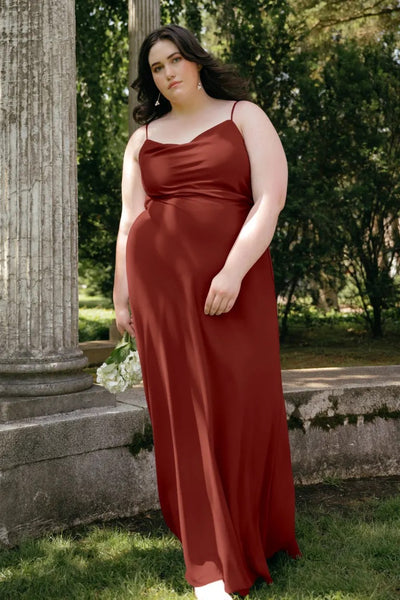 A woman in a Bianca - Bridesmaid Dress by Jenny Yoo, red evening gown with a cowl neck standing next to a column in a park setting.