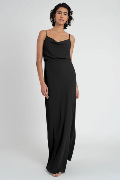 A woman in a sleek black Bianca bridesmaid dress by Jenny Yoo posing against a neutral background.