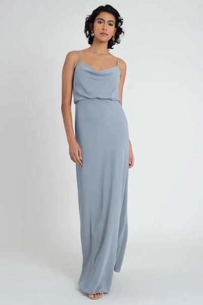 Woman posing in a sleeveless light blue Bianca bridesmaid dress with a draped cowl neck by Jenny Yoo, on a plain background from Bergamot Bridal.