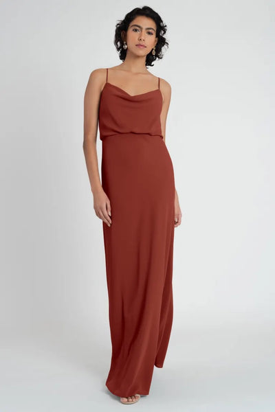 A woman posing in a sleeveless terracotta Bergamot Bridal Bianca bridesmaid maxi dress by Jenny Yoo.