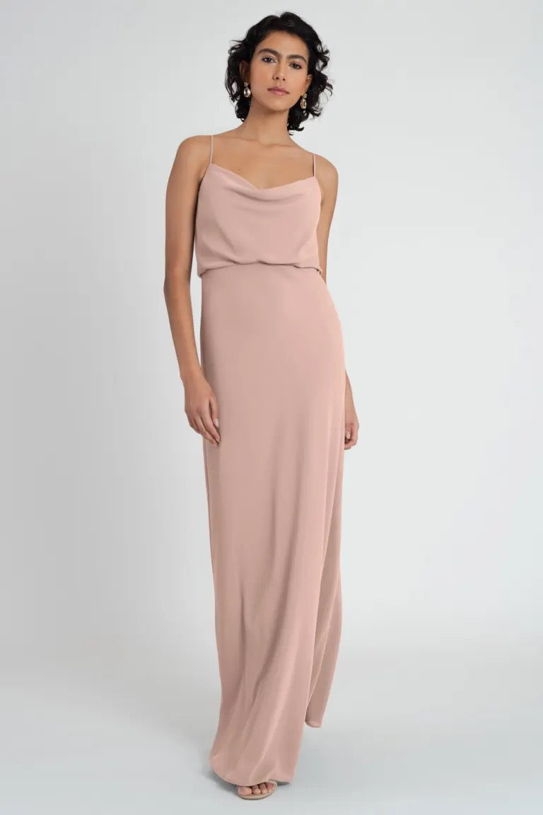 A woman stands wearing a long, pale pink Bianca bridesmaid dress with spaghetti straps from Bergamot Bridal.