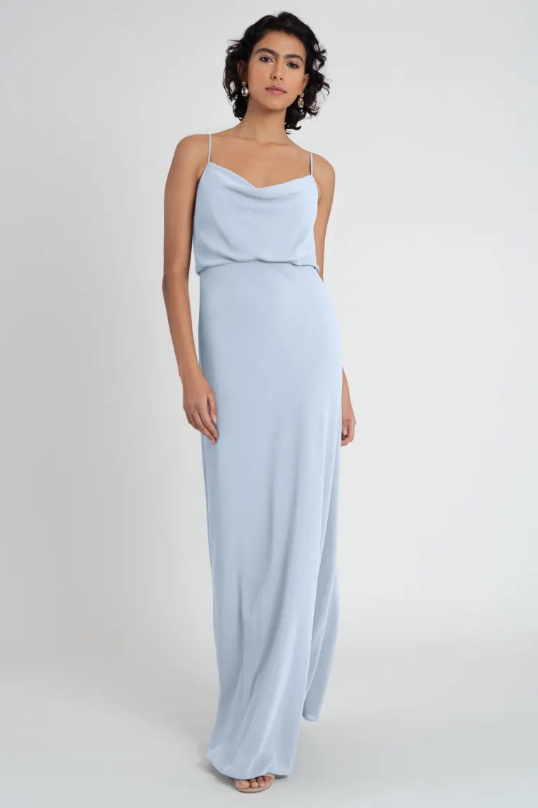 Woman in a pale blue, sleeveless maxi Bianca bridesmaid dress by Jenny Yoo made of pebbled crepe fabric, standing against a neutral background.